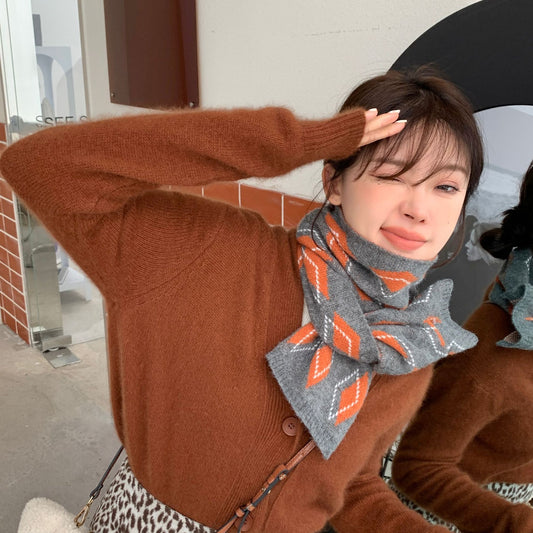A person wearing a brown cardigan and a knitted scarf with a geometric pattern in gray, orange, and blue colors.