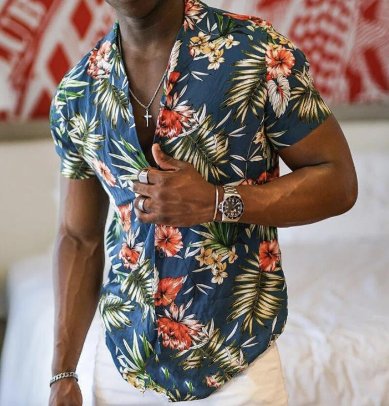A man wearing a green Urban Crest button-up shirt with a floral pattern consisting of leaves and flowers, in a room with a red and white patterned wall.