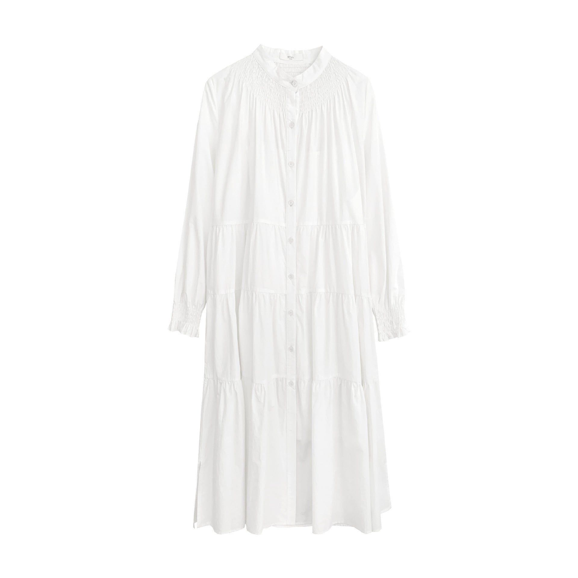 A woman sitting at a table wearing a white midi-length pleated dress with a round neckline and long sleeves.