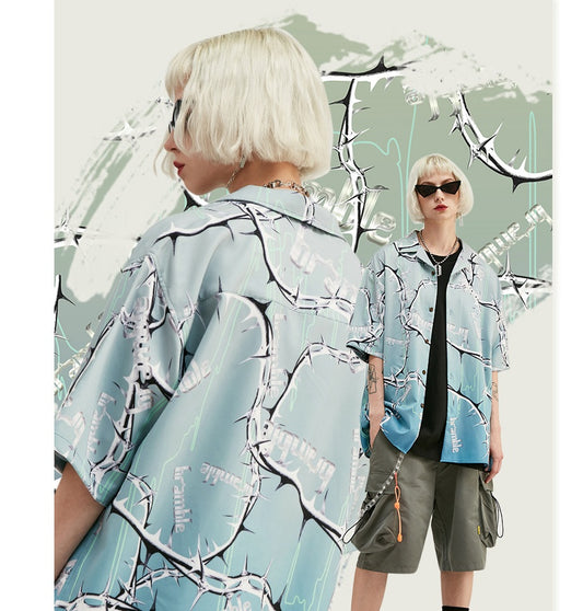 Two individuals wearing loose-fitting, button-up shirts with a tropical and pixelated pattern, designed for a casual and streetwear-inspired look.