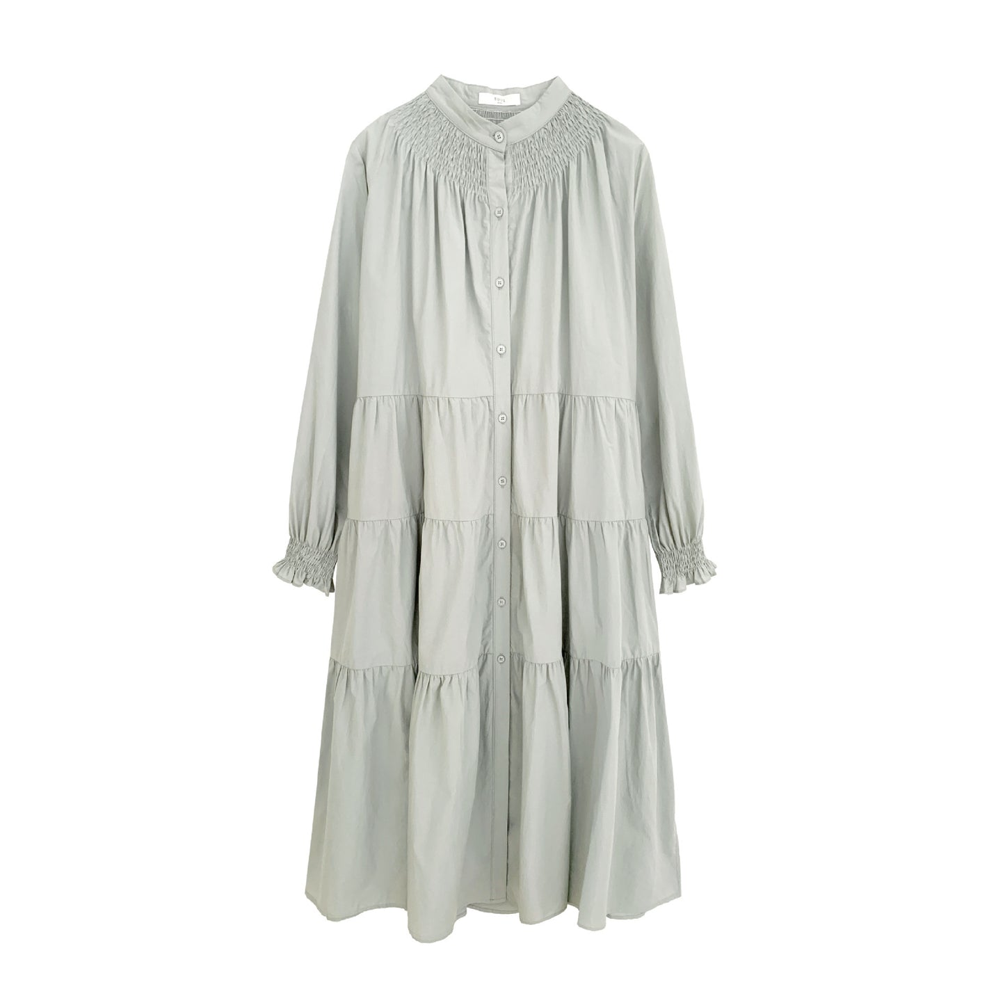 A woman sitting at a table wearing a white midi-length pleated dress with a round neckline and long sleeves.