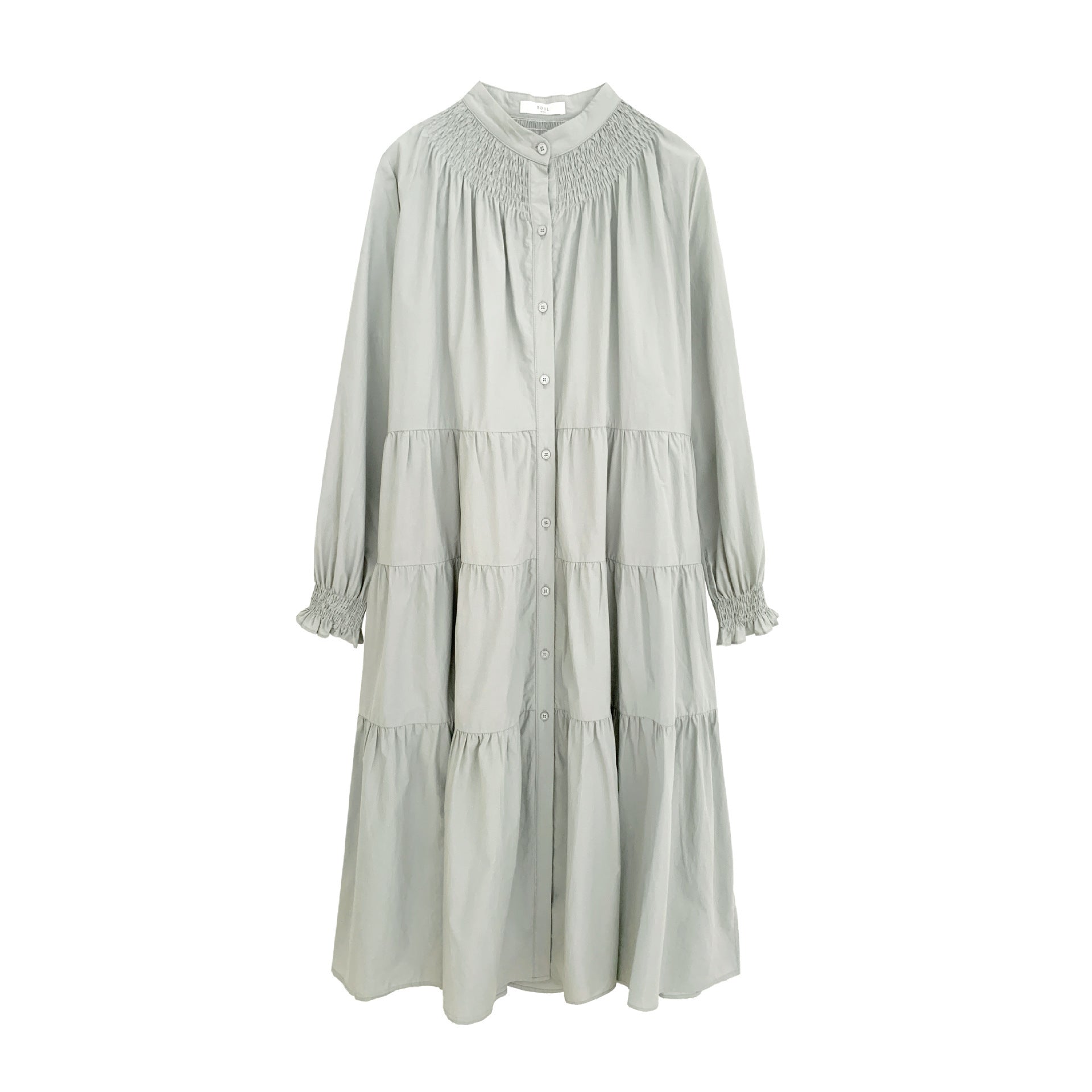 A woman sitting at a table wearing a white midi-length pleated dress with a round neckline and long sleeves.