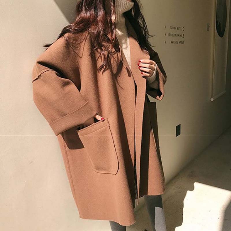 A person wearing a beige Urban Ember Wool Wrap coat with a turtleneck sweater underneath, standing indoors.
