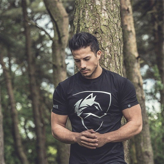 A man standing outdoors wearing a black Iron Raven Gymwear t-shirt with a logo on the front.