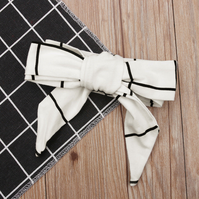 A long-sleeve plaid dress and matching headband laid out on a wooden surface, predominantly beige and black in color.