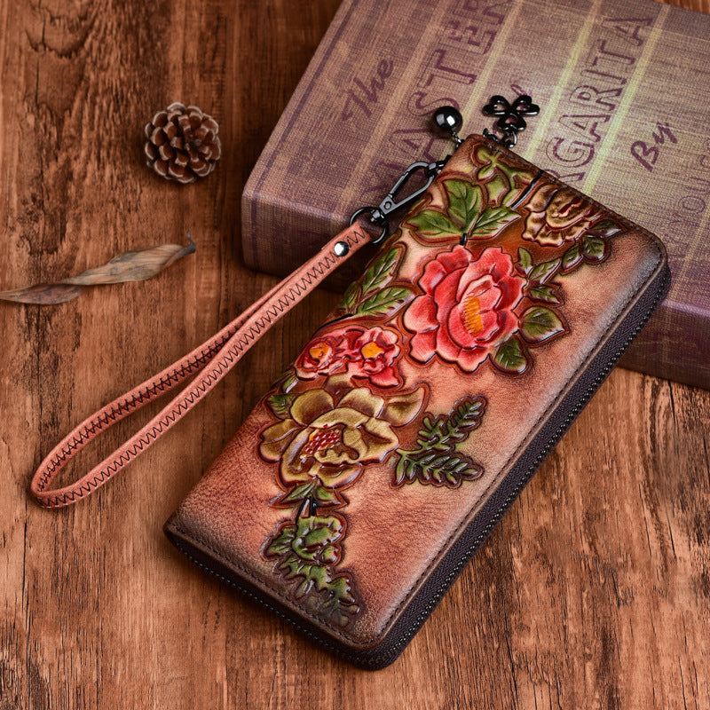 A brown wallet with floral embossing, placed on a wooden surface next to a book and a pine cone.