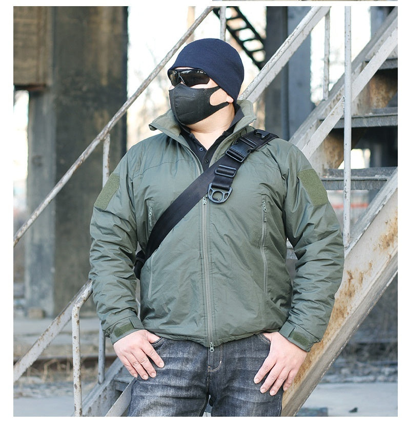 A person wearing a camouflage waterproof coat with a hood, sunglasses, and a beanie. They are standing in a dilapidated building setting.