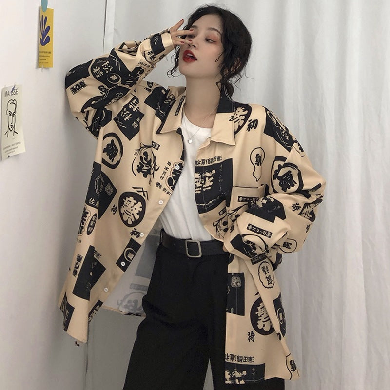 A woman wearing a beige long-sleeved shirt with Harajuku-inspired patterns and text, paired with black pants.