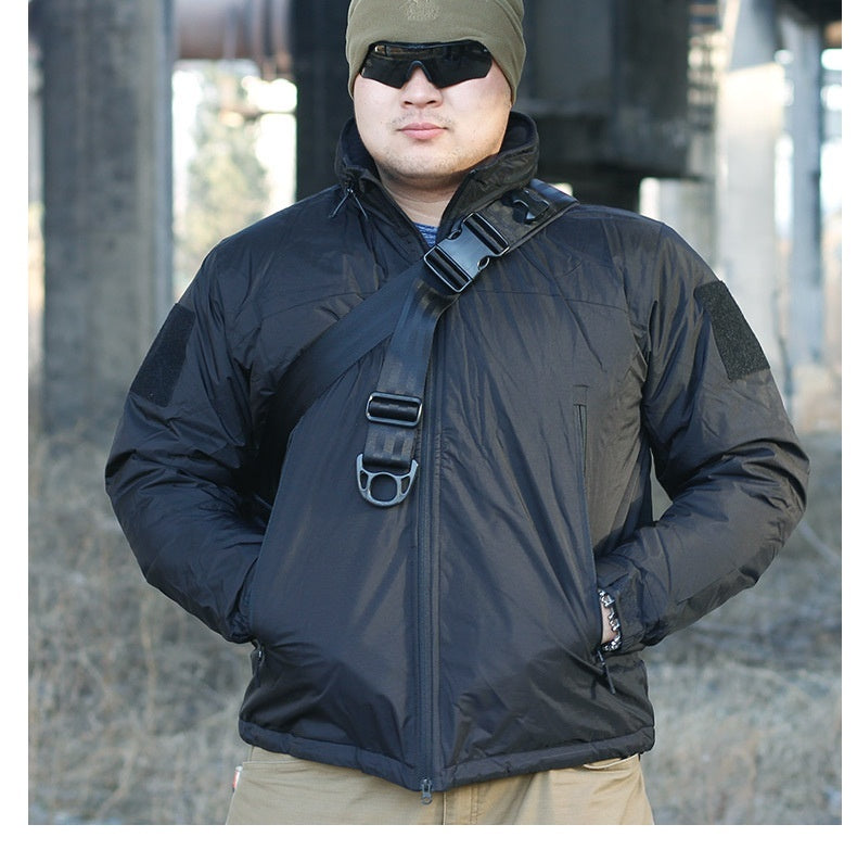 A person wearing a camouflage waterproof coat with a hood, sunglasses, and a beanie. They are standing in a dilapidated building setting.