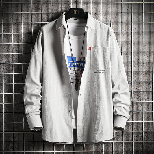 A male fashion model wearing a white Urban Wave men's fashion top with a lapel collar, long sleeves, and a slim fit. The top is displayed in an urban setting with a tiled wall in the background.