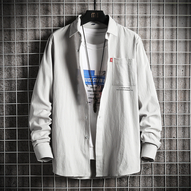 A male fashion model wearing a white Urban Wave men's fashion top with a lapel collar, long sleeves, and a slim fit. The top is displayed in an urban setting with a tiled wall in the background.