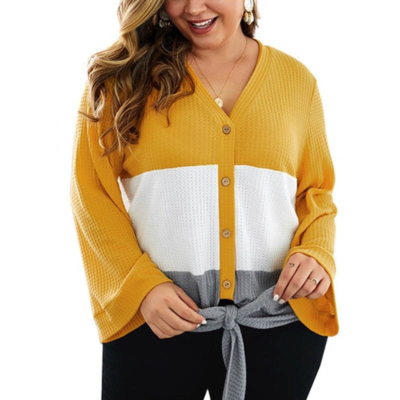 A female model wearing a color-blocked Urban Flow Relaxed Slim Sweater in white, yellow, and gray colors, paired with black pants and a gray sash.