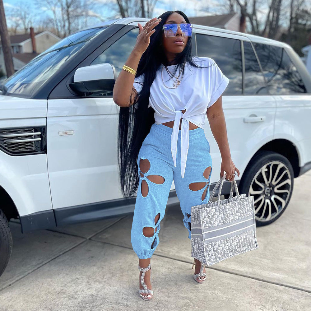 Woman in white top and blue jeans standing next to a white SUV, holding a handbag.