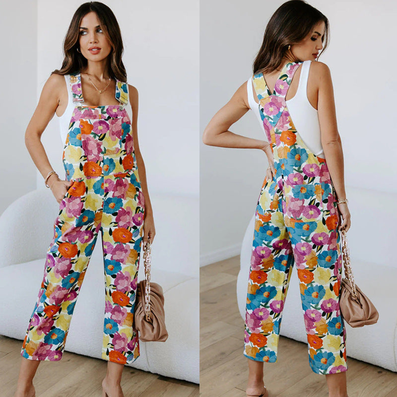 A model wearing a sleeveless, straight-leg floral print jumpsuit in a room with a white background.