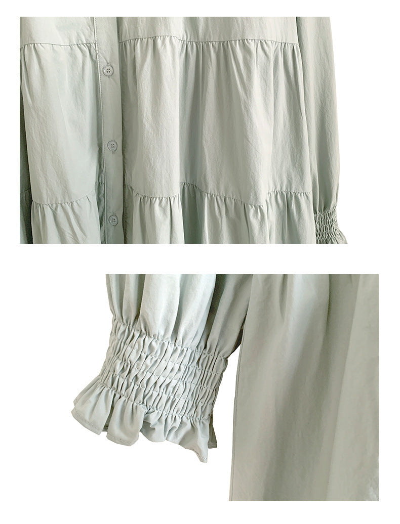 A woman sitting at a table wearing a white midi-length pleated dress with a round neckline and long sleeves.