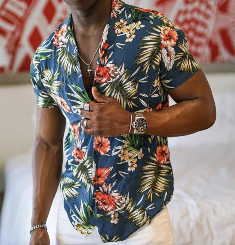 A man wearing a green Urban Crest button-up shirt with a floral pattern consisting of leaves and flowers, in a room with a red and white patterned wall.