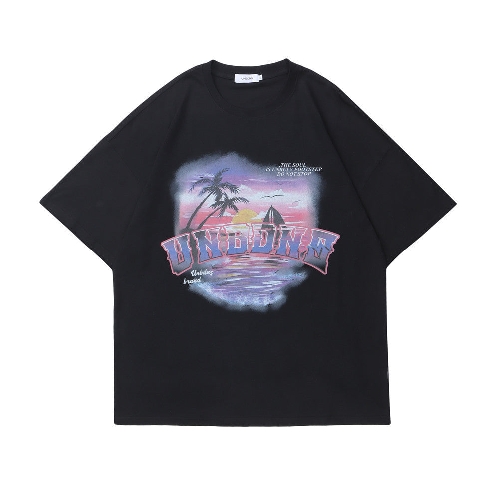 A person wearing a black short-sleeved t-shirt with a seaside landscape print, including a palm tree and a sunset, paired with dark pants and a purple cap.