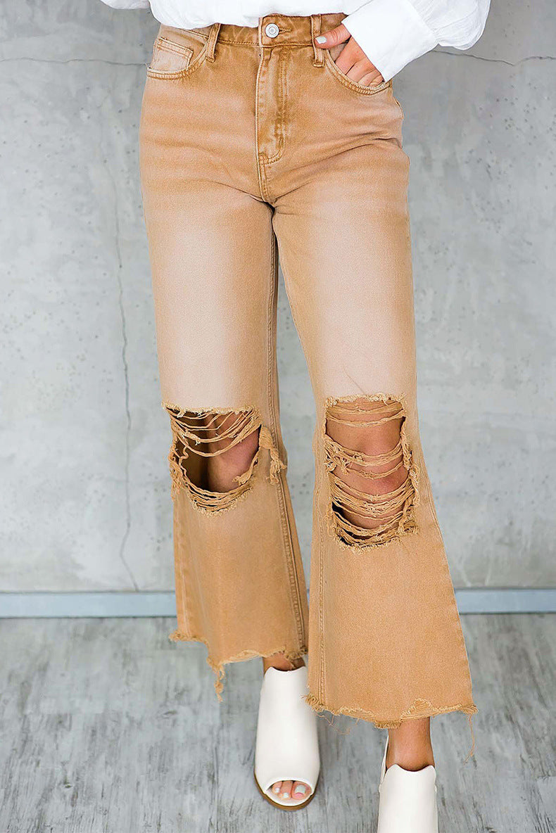 Tan flared jeans with rips worn by a person on a gray background