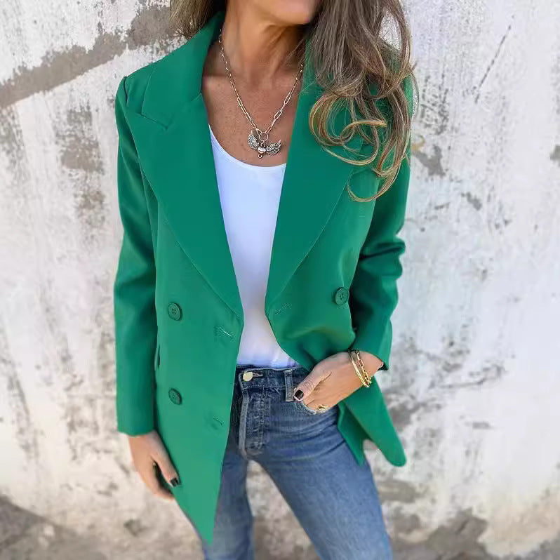 A woman wearing a green Urban Grace Lapel Jacket with a white top and blue jeans. She has accessorized with a necklace and has convenient pockets on the jacket.