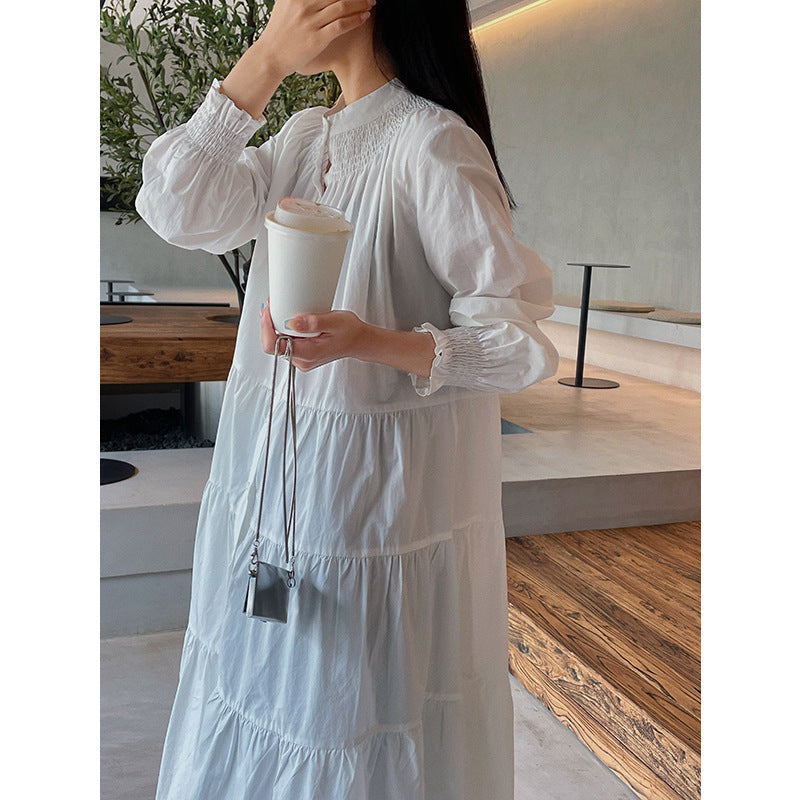 A woman sitting at a table wearing a white midi-length pleated dress with a round neckline and long sleeves.