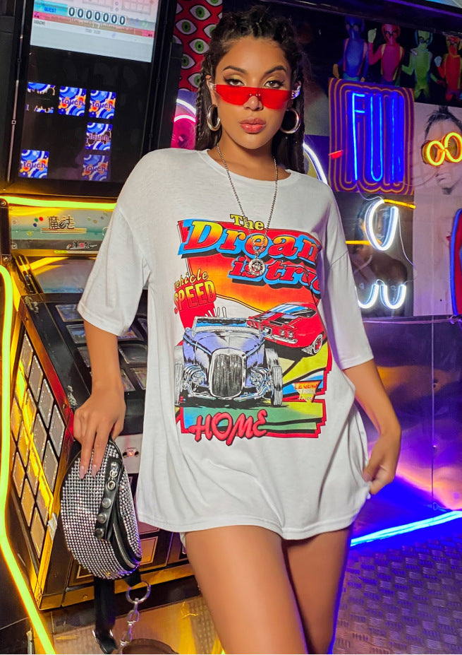 A woman wearing an oversized top with a graphic print, paired with shorts and red sunglasses.
