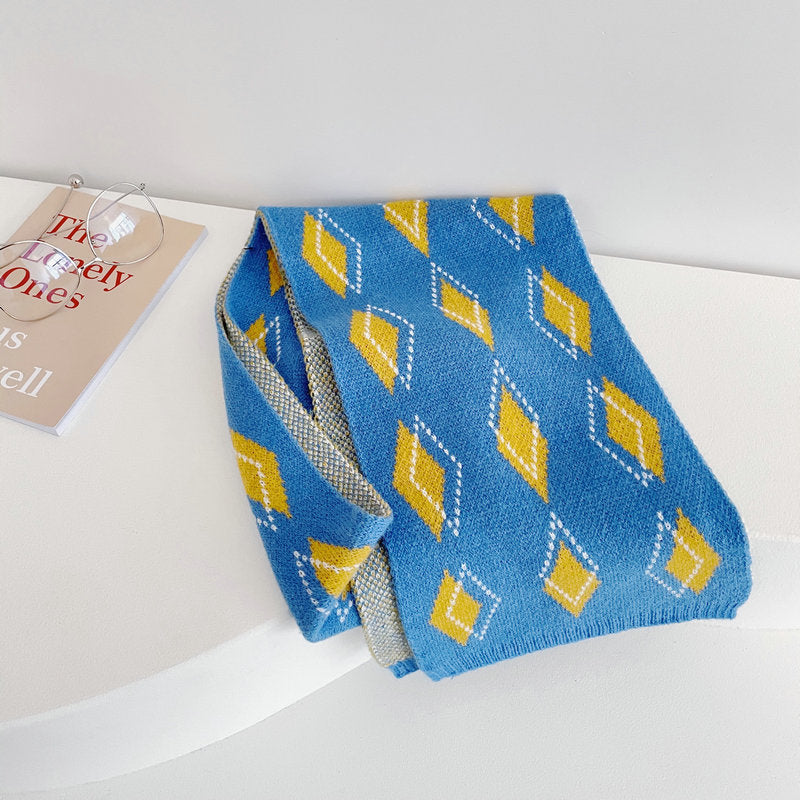 A person wearing a blue cardigan and a knitted scarf with a geometric pattern in gray, orange, and blue colors.