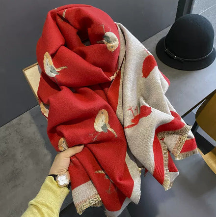 A green cashmere shawl with a bird pattern, held open by a hand, displayed against a grey background.