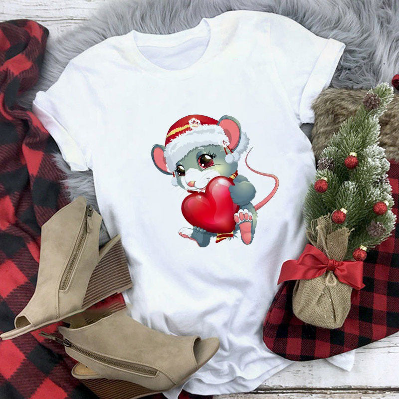 White t-shirt with a Christmas-themed design of a mouse in a Santa hat holding a heart, placed on a checkered fabric background with boots and a small tree.