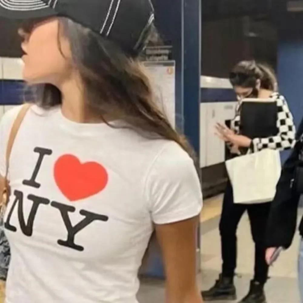 A person wearing a white crop top with the text 'I ❤️ NY' printed on the front.