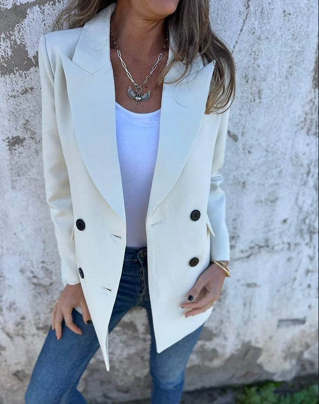 A woman wearing a white Urban Grace Lapel Jacket with a white top and blue jeans. She has accessorized with a necklace and has convenient pockets on the jacket.
