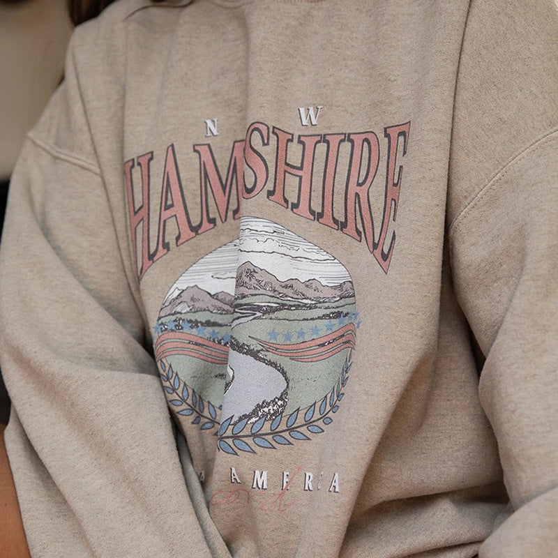 A woman sitting on a bench wearing a beige round neck sweatshirt with a printed design.