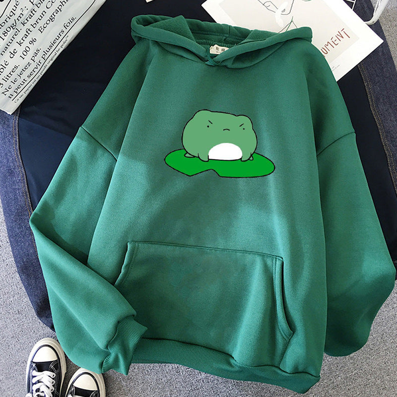 A green hooded sweatshirt with a bold green frog print on the front, laid flat on a surface with a pair of shoes in the background.