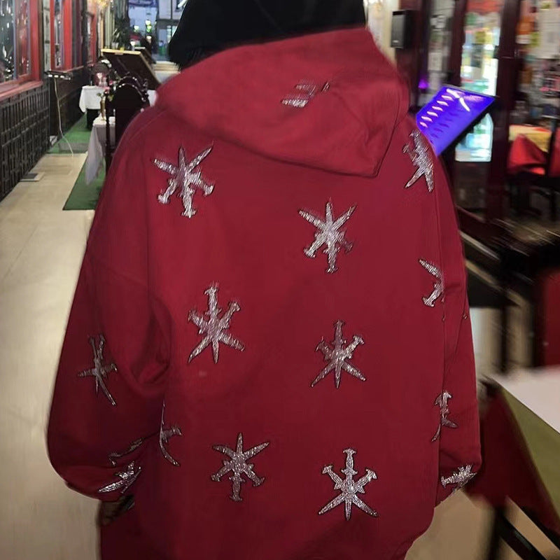 A person wearing a red zip hoodie with a geometric rhinestone pattern, in front of a backdrop featuring gothic-style artwork.