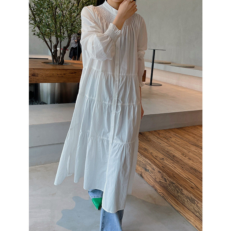A woman sitting at a table wearing a white midi-length pleated dress with a round neckline and long sleeves.