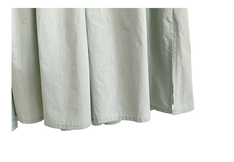 A woman sitting at a table wearing a white midi-length pleated dress with a round neckline and long sleeves.