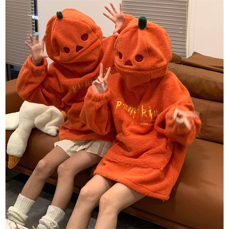 Two children wearing orange pumpkin-themed robes sitting on a couch.