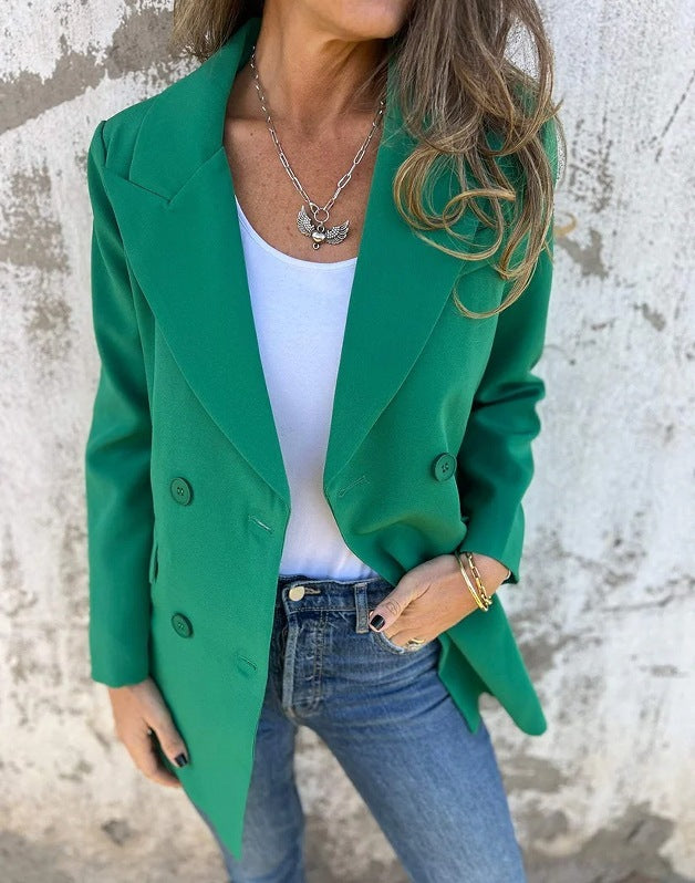 A woman wearing a green Urban Grace Lapel Jacket with a white top and blue jeans. She has accessorized with a necklace and has convenient pockets on the jacket.