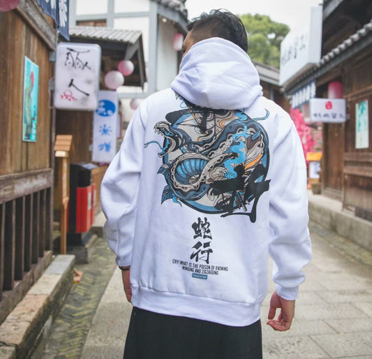 A person wearing a white urban sweatshirt with a unique Chinese script and graphic design on the back, walking in a street with oriental decorations.