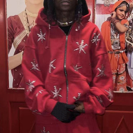 A person wearing a red zip hoodie with a geometric rhinestone pattern, in front of a backdrop featuring gothic-style artwork.