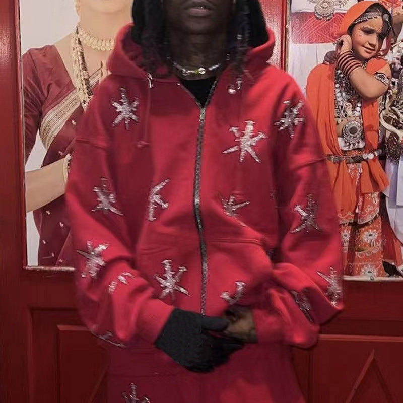 A person wearing a red zip hoodie with a geometric rhinestone pattern, in front of a backdrop featuring gothic-style artwork.