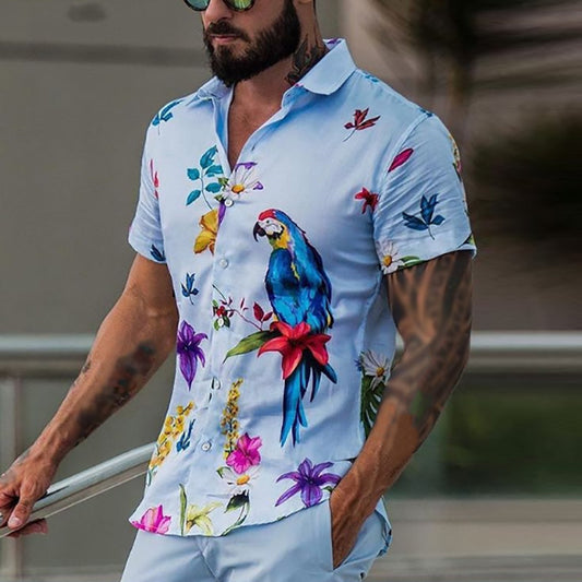 A man wearing a short-sleeved button-up shirt with a tropical print, featuring a parrot and various flowers on a light blue background.