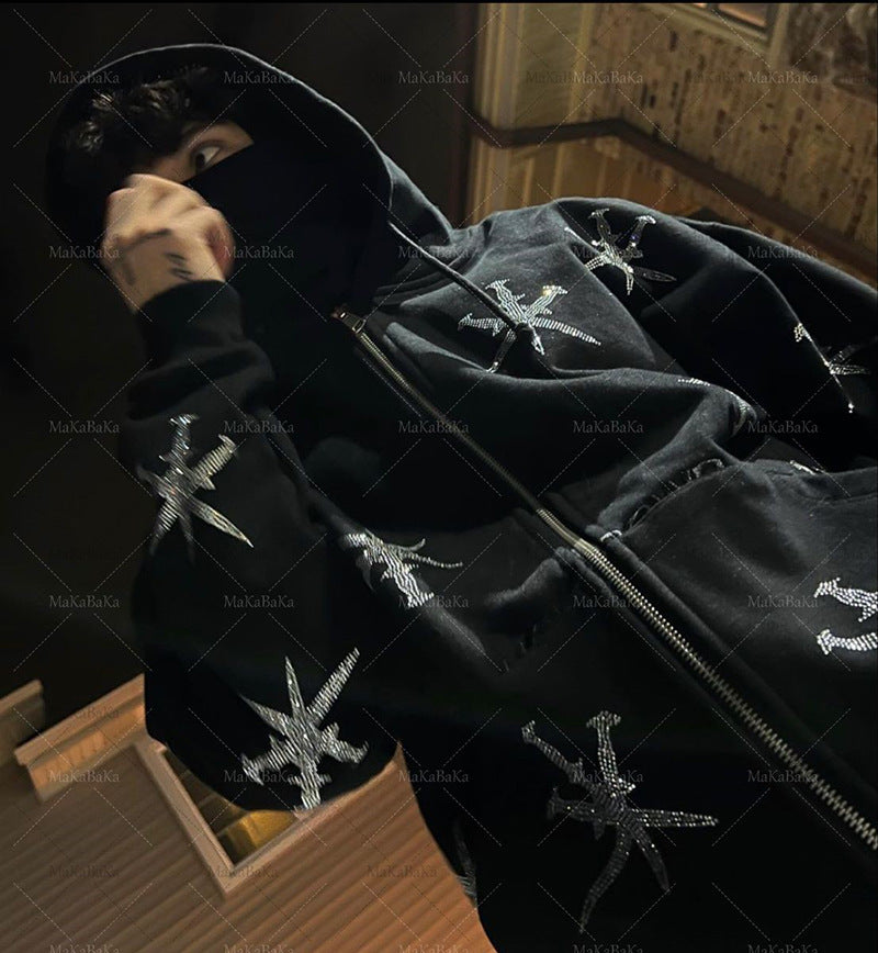 A person wearing a black zip hoodie with a geometric rhinestone pattern, in front of a backdrop featuring gothic-style artwork.