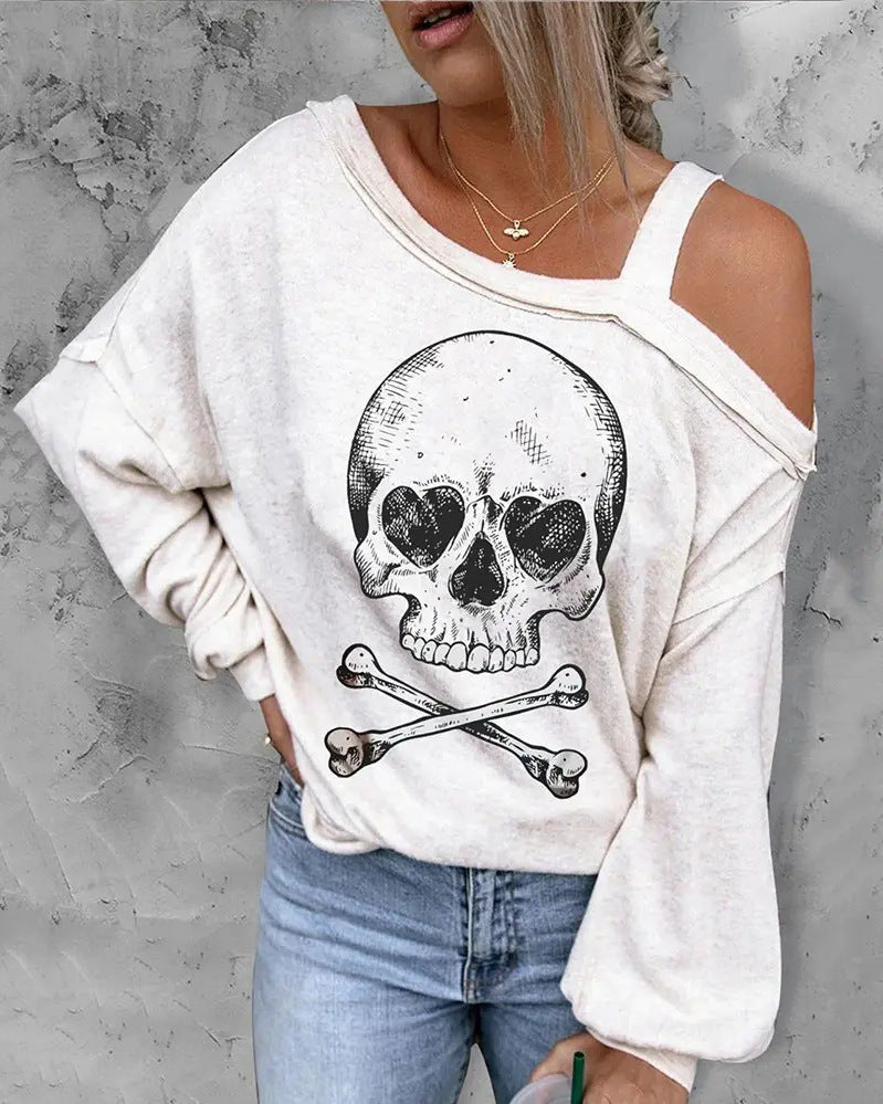 Person wearing a white sweatshirt with a skull and crossbones design against a gray concrete wall.