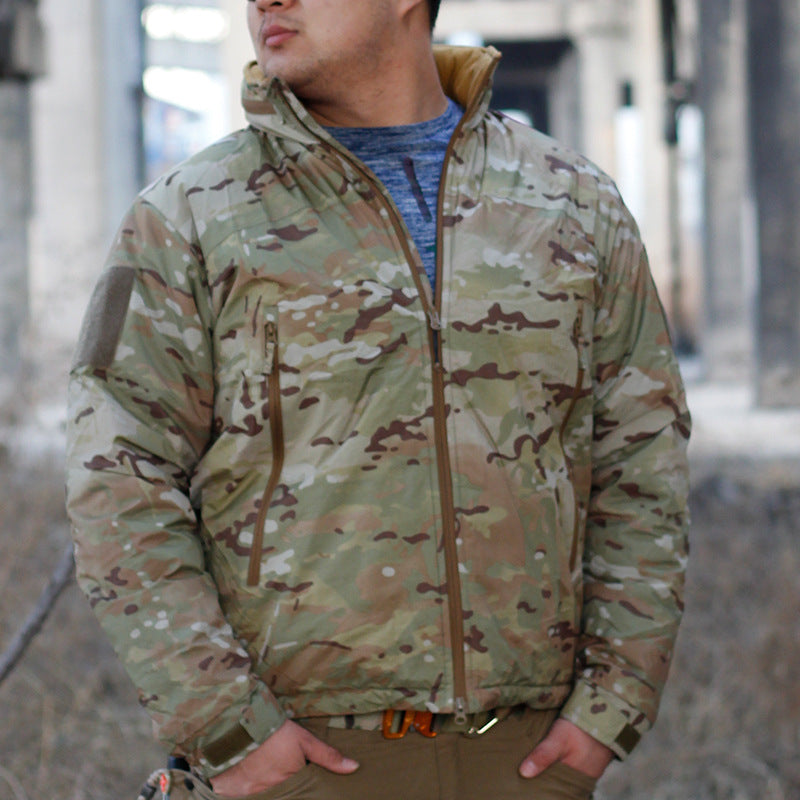 A person wearing a camouflage waterproof coat with a hood, sunglasses, and a beanie. They are standing in a dilapidated building setting.