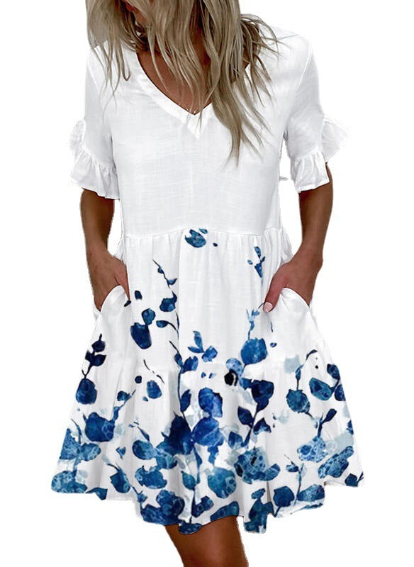 A woman wearing a white knee-length dress with blue floral print, V-neckline, and lotus leaf short sleeves.