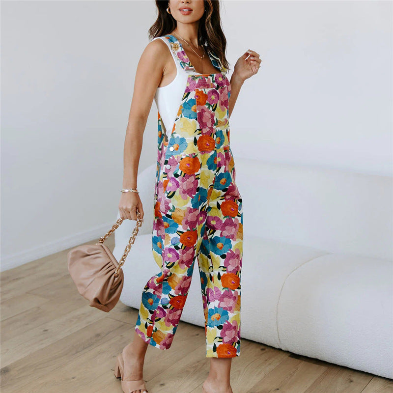A model wearing a sleeveless, straight-leg floral print jumpsuit in a room with a white background.