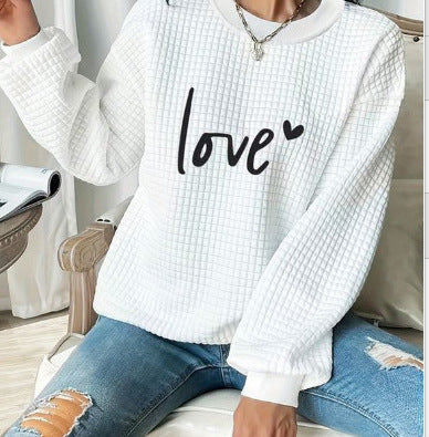 White textured sweater with 'love' print worn by a person sitting on a chair.