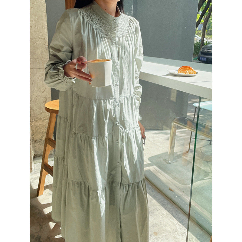 A woman sitting at a table wearing a white midi-length pleated dress with a round neckline and long sleeves.