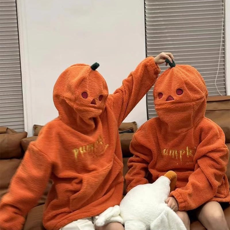 Two children wearing orange hoodies with pumpkin designs and 'pumpkin' text, sitting on a couch.