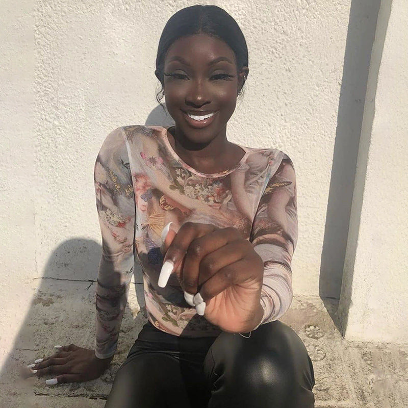 A woman modeling a long sleeve bodysuit with a printed design, wearing denim pants and accessorized with a watch and earrings.